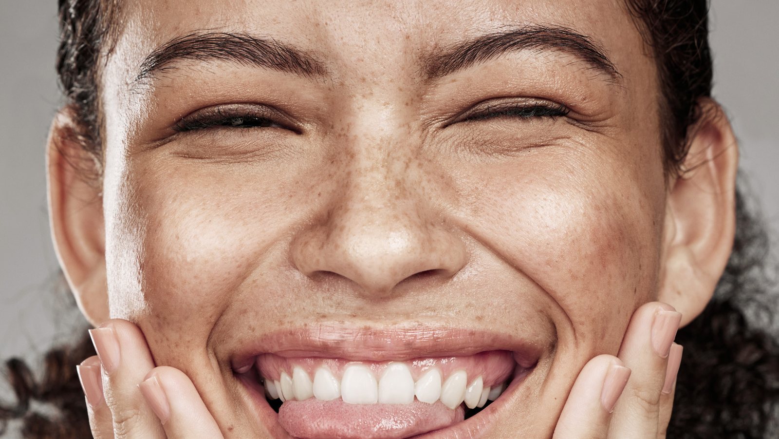 Freckled woman laughing, hands on her cheeks